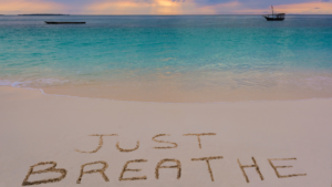 'just breathe' written in sand