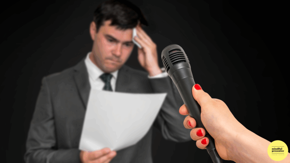 nervous male presenter mopping brow in front of a microphone