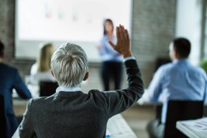 woman holding her hand up to ask presenter a question