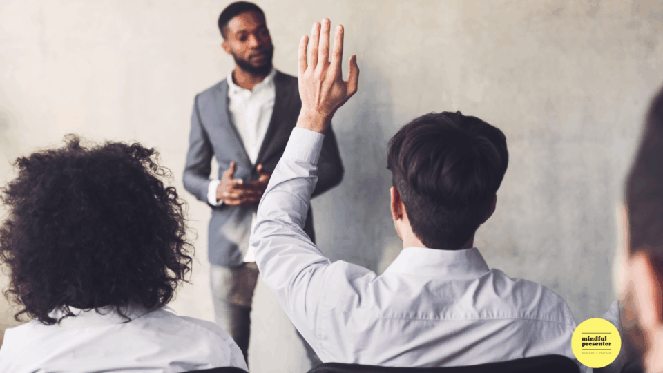 man with arm raised in audience to ask question