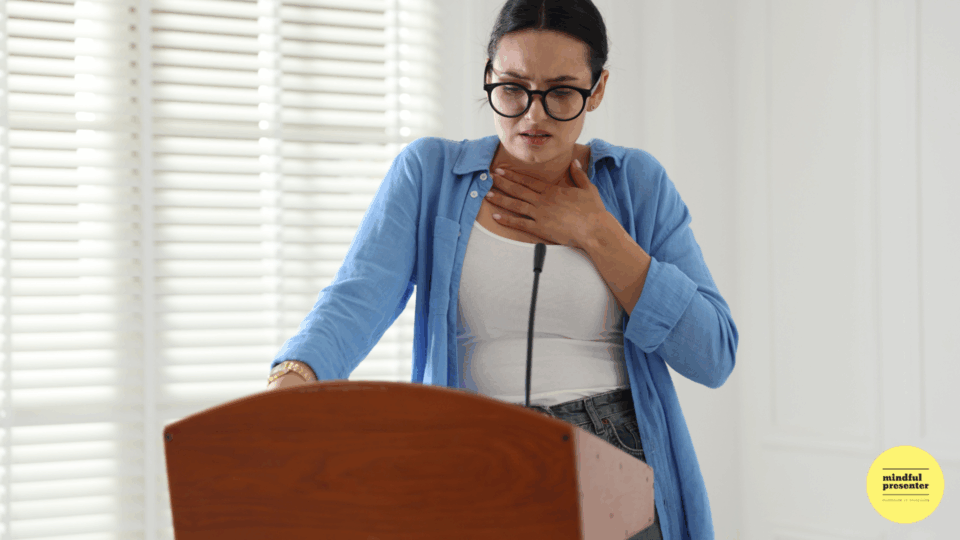 Woman standing behind lectern holding chest looking nervous