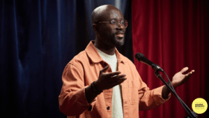 man speaking into microphone, arms wide open