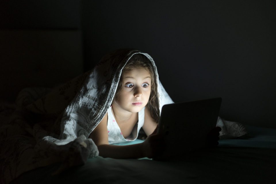 girl reading story under blanket on tablet