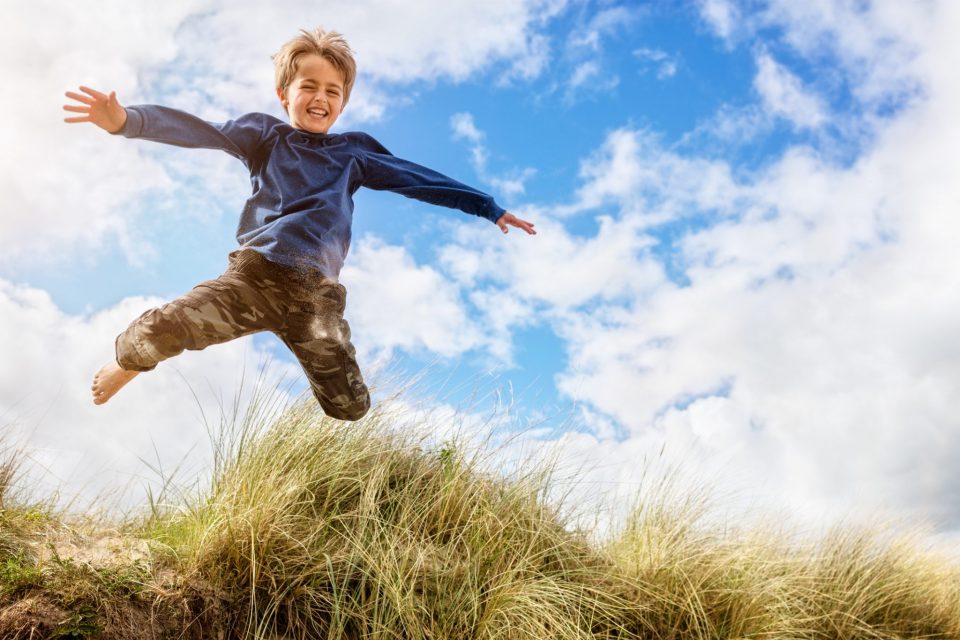 Boy jumping over sand dunes on beach vacation