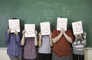 Five students holding faces of different emotions they have from worry to happy