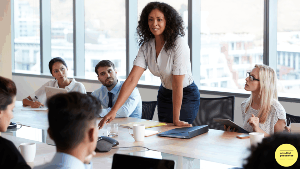 woman speaking in meeting room leaning forward with both hands on table