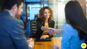 Two women shaking hands in a meeting with a man sitting next to them