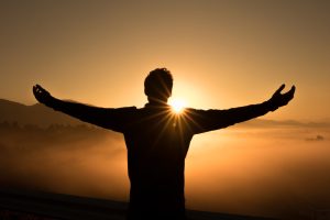 man holding arms out in sunset