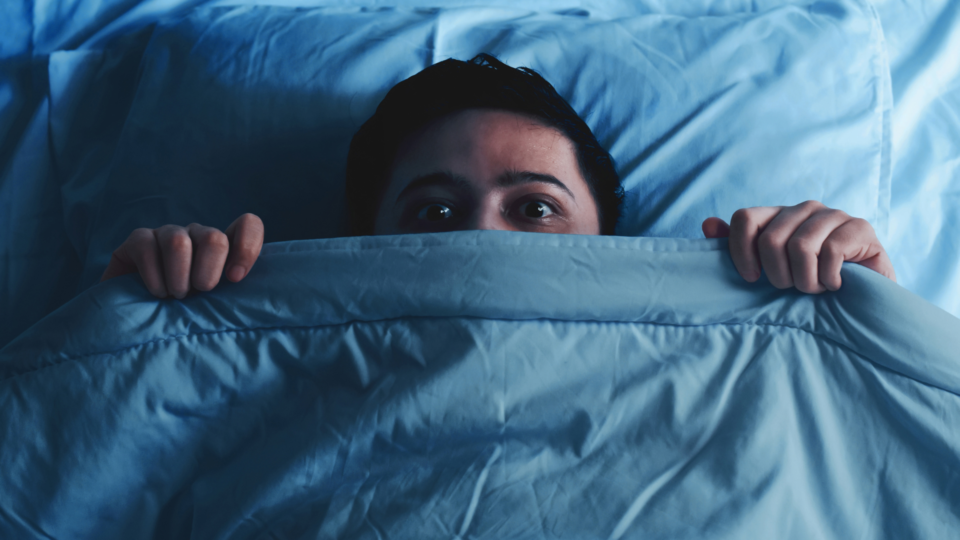 man looking scared under bed sheet