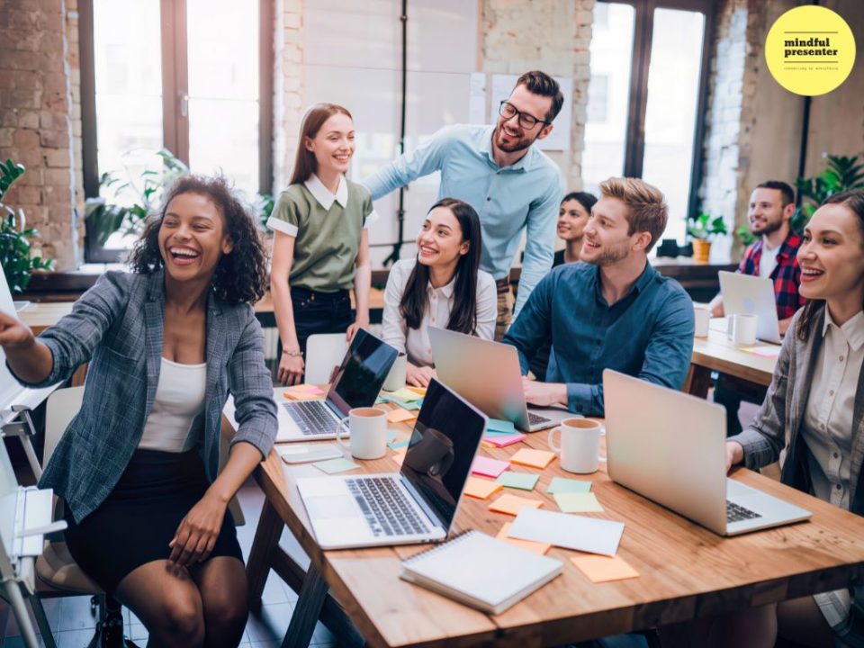 people smiling at laughing at work with laptops open in meeting