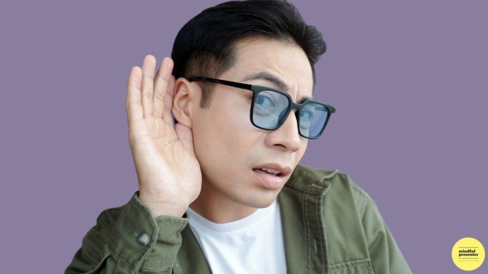 man wearing glasses holding is hand to his ear to listen