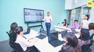 Man presenting using powerpoint in a meeting with everyone with laptops opening