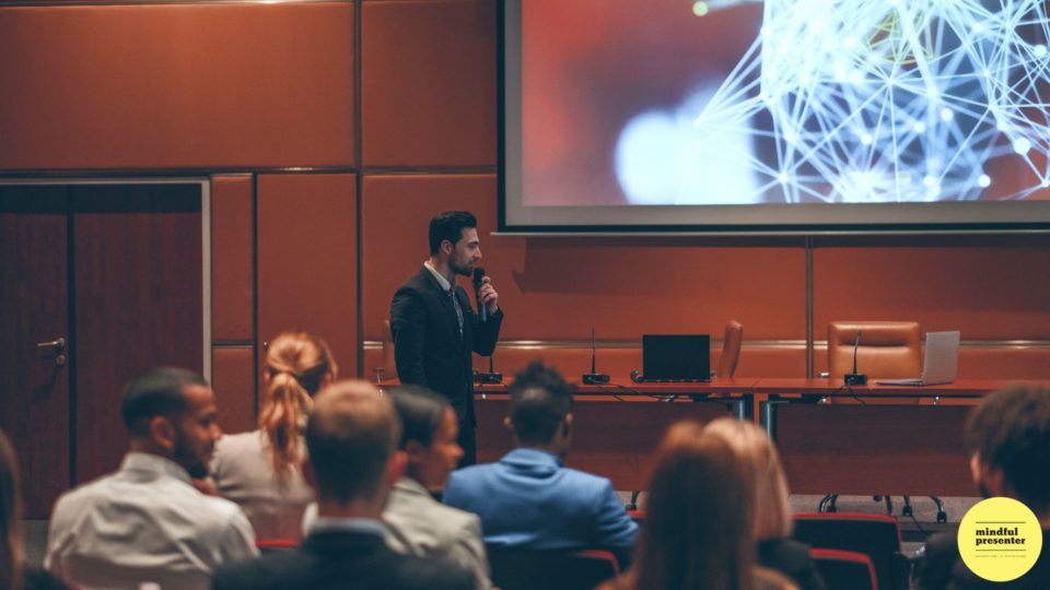 man speaking to audience holding a microphone